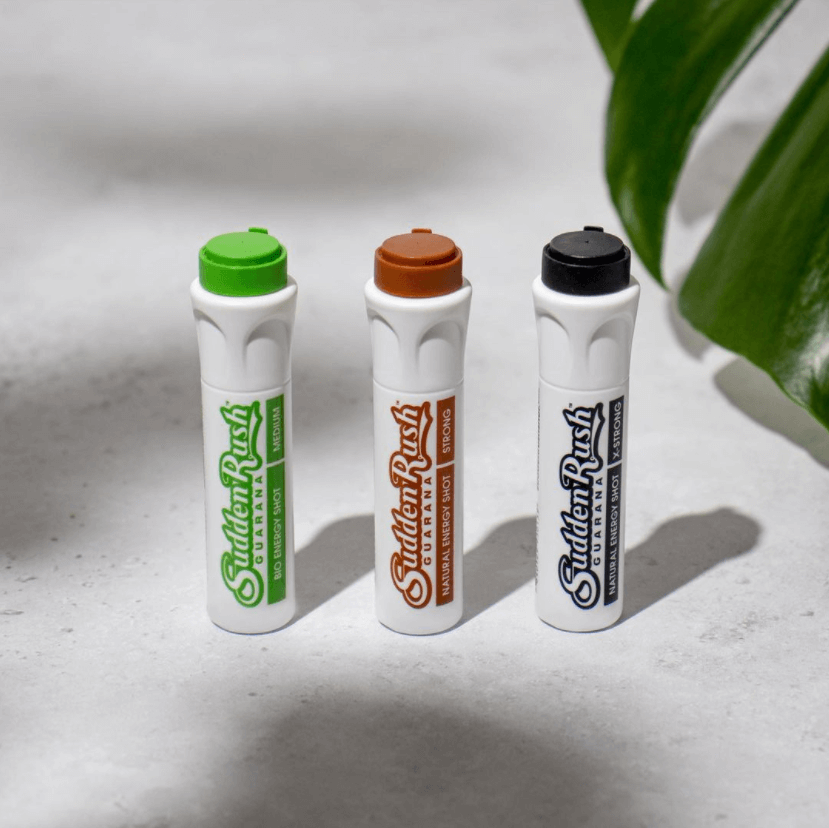 SuddenRush Guarana energy supplements in green, brown, and black vials on a light surface with a plant leaf in the background